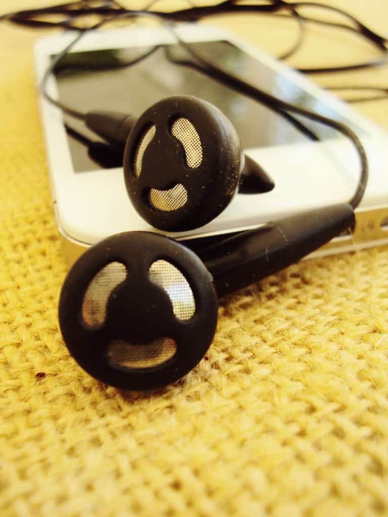 A close-up of black earphones with a smiling face design on the back, resting on a textured surface beside a white smartphone.