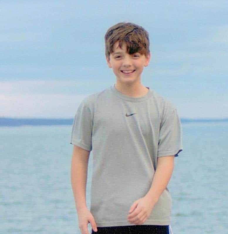 A cheerful young boy smiling at the camera with the ocean in the background.