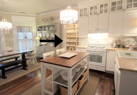 A cozy, well-lit kitchen with white cabinetry and a central island, featuring a dining area in the background.