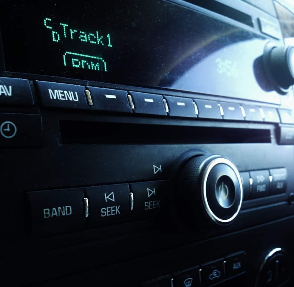 An angled view of a car stereo system displaying 'track 1' on its screen, with focus on the volume control knob.