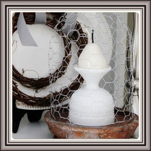 Image (12) A rustic candle holder with a tiered white candle inside, encased by a wire mesh, set against a backdrop of a wreath and subtle earthy tones, invoking a sense of country charm.