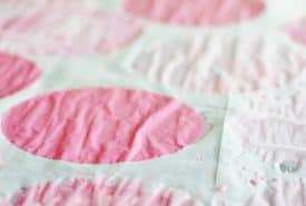 Close-up of a quilt featuring pink coffee filter flowers on a textured white background.