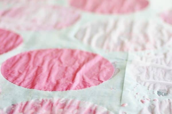 Close-up of a quilt featuring pink coffee filter flowers on a textured white background.