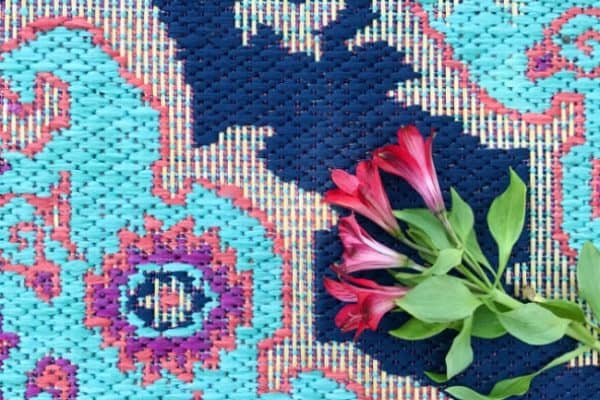 A vibrant floral fabric featuring a detailed pattern in shades of blue, pink, and purple, affordable for use in outdoor rugs, with a small bunch of fresh red flowers placed on top.