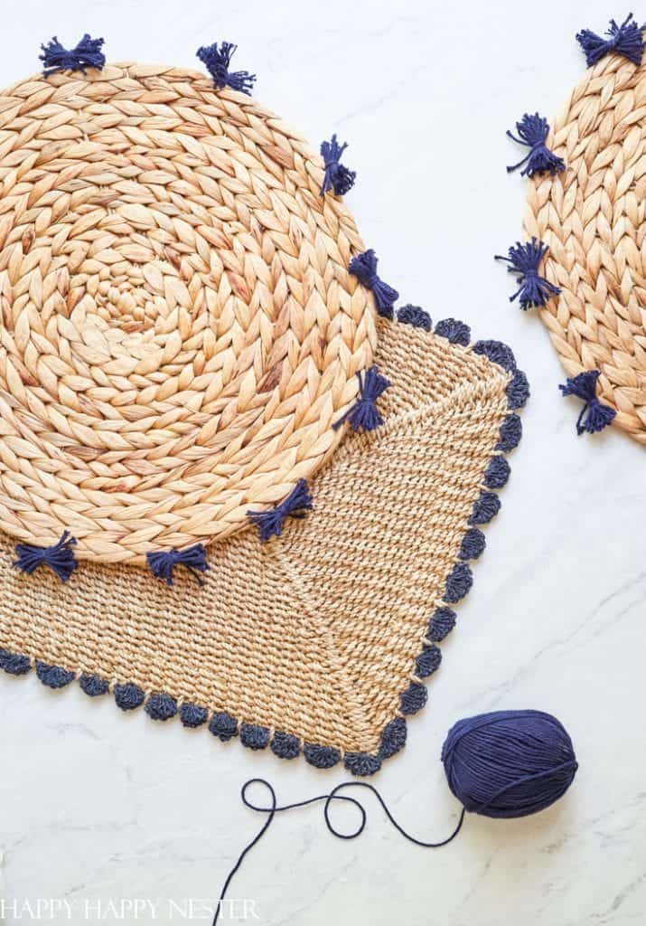 A decorative flat lay features woven straw placemats with dark blue tassels arranged on a light surface. A ball of dark blue yarn with a loose thread is placed in the bottom right corner. The image has a cozy, handmade feel.