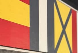 A close-up view of three nautical signal flags: the first has red and yellow horizontal stripes, the second has vertical stripes in black, white, and black, and the third is yellow with a black diagonal X.