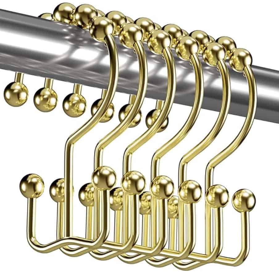 Several gold shower curtain hooks with ball-shaped ends hang on a silver metal rod, neatly aligned and overlapping each other.