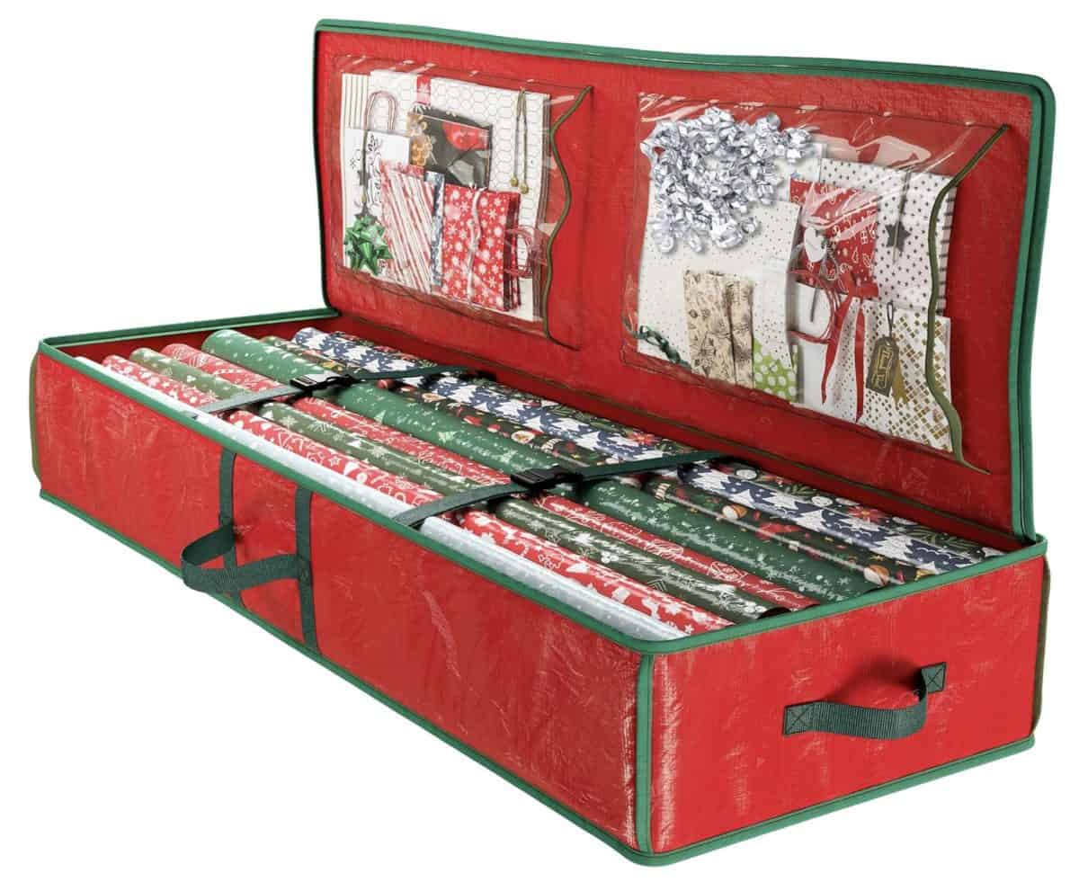 A red and green storage case holds multiple rolls of Christmas wrapping paper and has clear pockets in the lid containing gift bags, ribbons, and bows. The case is open and organized.