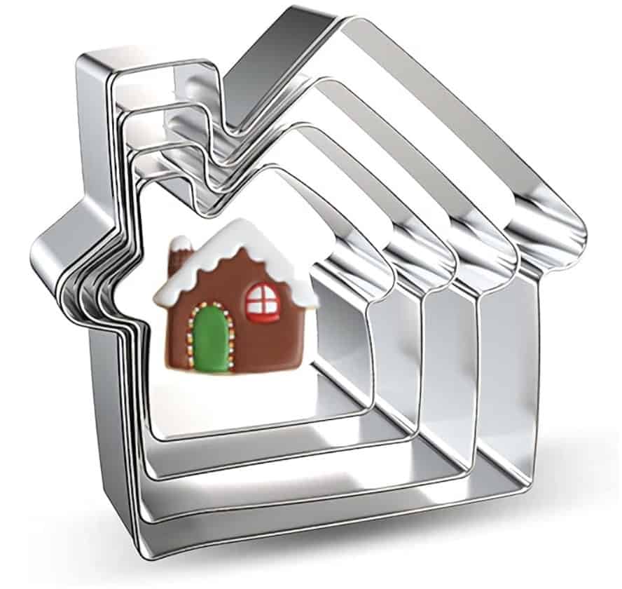 A set of nested house-shaped metal cookie cutters with a small decorated gingerbread house cookie placed inside the smallest cutter.