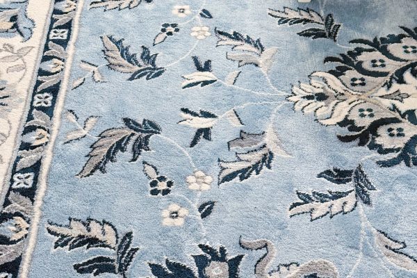 Detailed blue and white floral-patterned rug with a white-legged, blue-striped upholstered stool partially visible in the upper right corner.