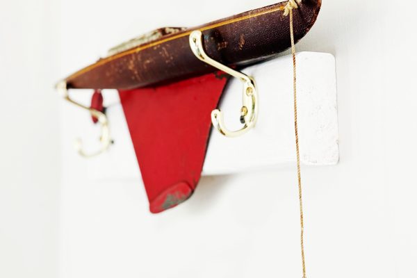 A decorative object shaped like a small red and brown boat with gold hooks is mounted on a white wall, with a string hanging from the front.