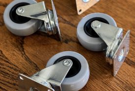 Five gray swivel caster wheels with metal brackets are arranged on a wooden floor.