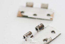 Two rusty, paint-chipped door hinge plates lying on a white surface, one in the foreground and one slightly out of focus in the background.