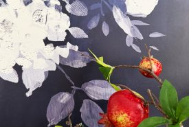 Red pomegranates and green leaves on branches in the foreground, with a purple background featuring white and light lavender floral patterns.