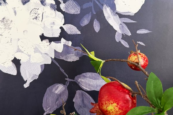 Red pomegranates and green leaves on branches in the foreground, with a purple background featuring white and light lavender floral patterns.