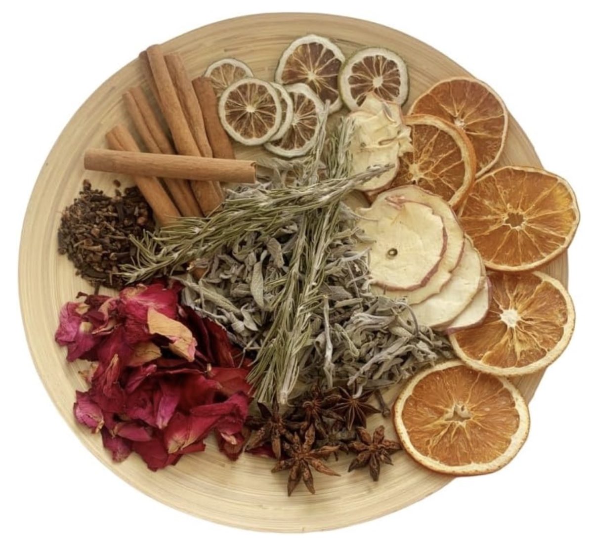 A round wooden plate with dried orange, lemon, apple slices, rose petals, star anise, cinnamon sticks, sage, rosemary, and cloves arranged in sections.
