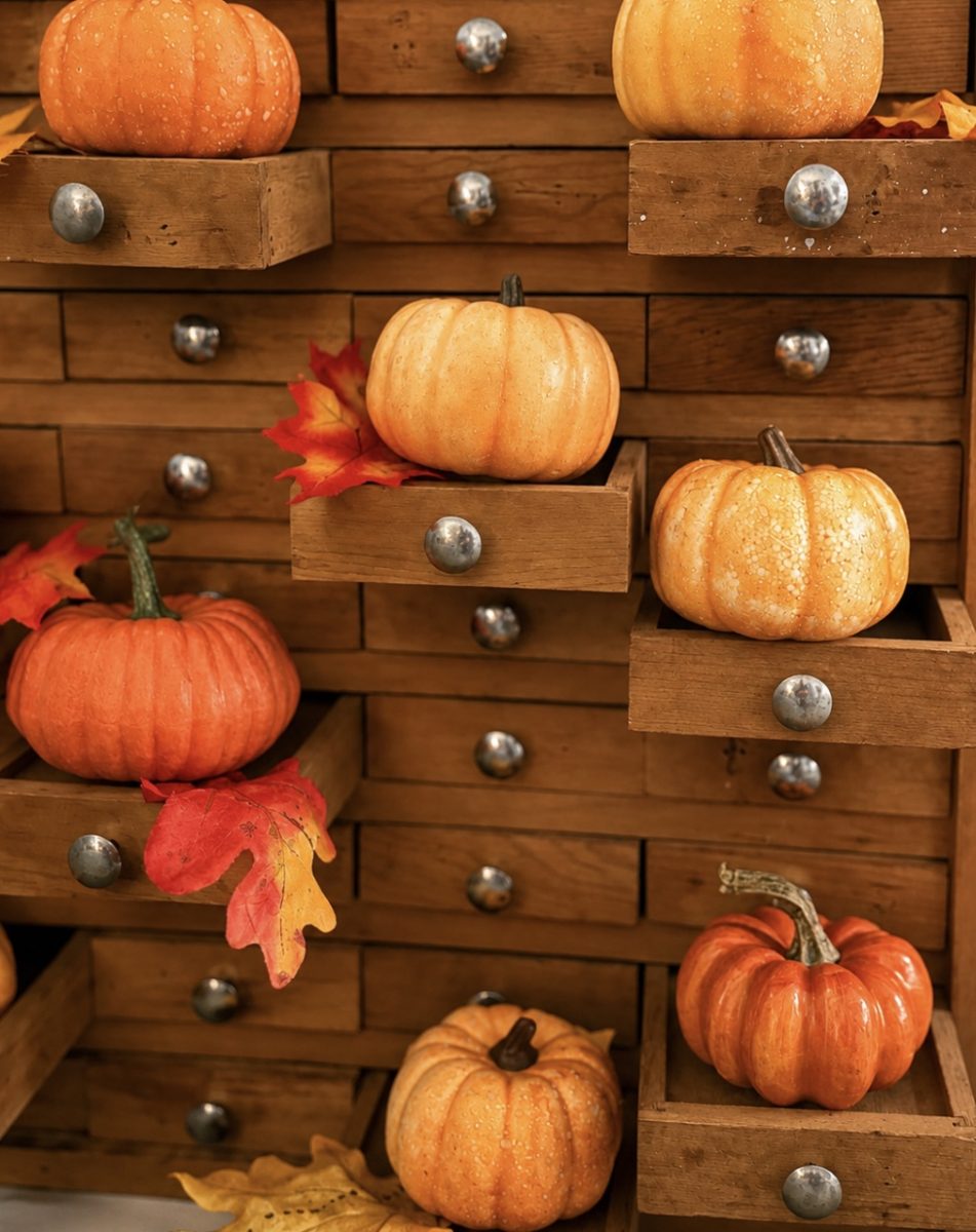 Mini orange pumpkins and autumn leaves are displayed on and inside the open drawers of a rustic wooden cabinet, creating a cozy fall decoration.
