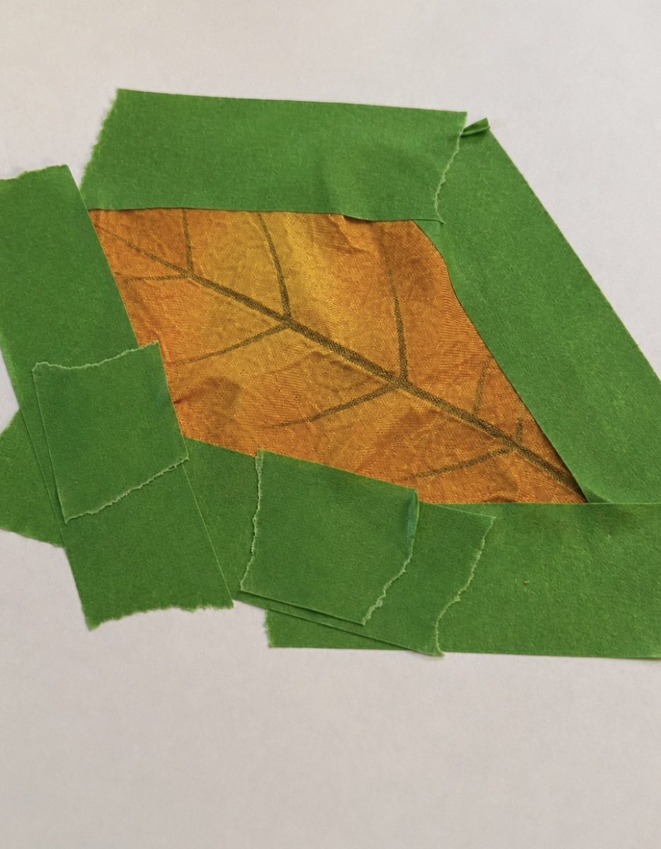 A piece of orange fabric with a leaf pattern is partially bordered by torn green tape on a plain white background.