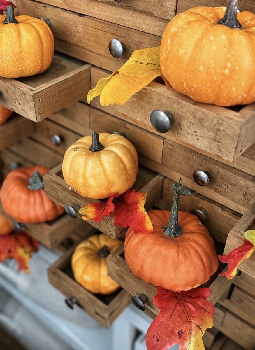 Small pumpkins and colorful autumn leaves are arranged on open wooden drawers, creating a festive fall display.