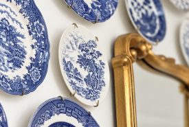 A collection of blue and white patterned ceramic plates displayed on a wall next to a gold-framed mirror.